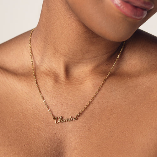 Close-up of a person's neck wearing an 18k gold plated necklace with the word "Dlamini" spelled out in cursive letters.