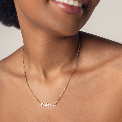 Close-up of a person's neck wearing an 18k gold plated necklace with the word "Mokoena" spelled out in cursive letters.