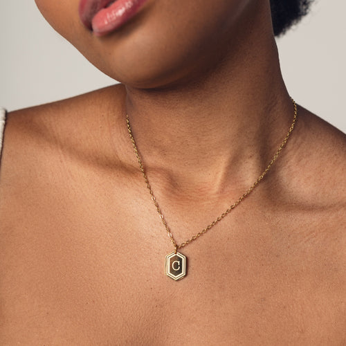 A close-up image of a woman wearing a delicate 18k gold  plated chain necklace with a hexagonal pendant. The pendant features a bold, engraved letter "C" in the center. 